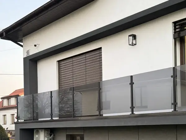 Nowoczesna balustrada z matowego szkła i czarnych słupków w kolorze RAL 9005, odbijająca drzewa.