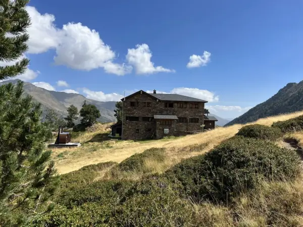 Refugio Comapedrosa, un edificio de piedra en un paisaje montañoso con hierba seca y cielo azul.