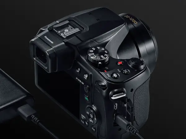 Czarny aparat Panasonic Lumix FZ82 z obiektywem 20-1200, podłączony do ładowarki.