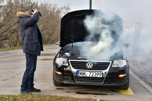 Mężczyzna z przerażeniem patrzy na dymiący silnik swojego Volkswagena. To typowe objawy zatarty silnik.