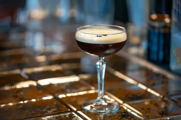 Elegancki drink z espresso, z gęstą pianką na wierzchu, stoi na błyszczącym blacie.