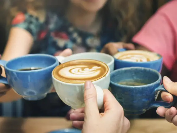 Vier Hände halten bunte Kaffeetassen. Der Kaffee reizt die Blase, aber der Genuss ist es wert.