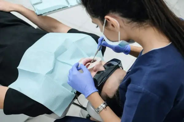 Dentystka w rękawiczkach zakłada pacjentowi na zęby materiał, być może formokrezol, do leczenia kanałowego.