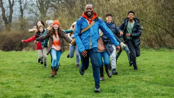 Lehrer und Schüler rennen lachend über eine grüne Wiese. Perfekt, um eine Klassenfahrt zu organisieren und Abenteuer zu erleben!
