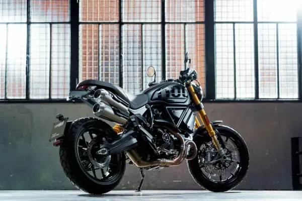 Czarny motocykl Ducati Scrambler 1100 Sport Pro, jeden z najlepszych motocykli, stoi przed industrialnymi oknami.