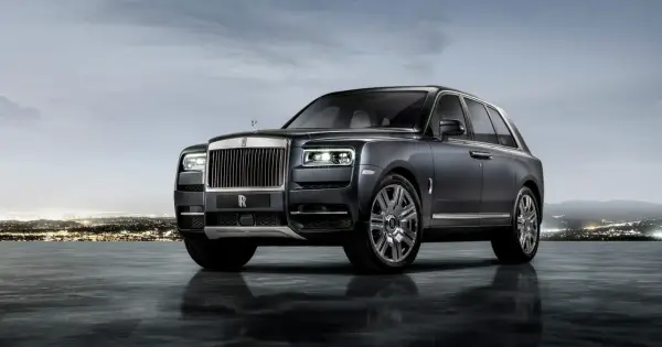 Elegancki Rolls-Royce SUV w ciemnym kolorze, lśniącym na tle nocnego miasta i gór.