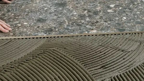 Pose de mortier pour un double encollage de carrelage. Les mains d'un carreleur préparent la surface.