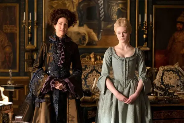 Due donne in abiti storici, una con capelli ricci e un vestito scuro elaborato, l'altra con capelli biondi raccolti e un abito verde chiaro. Le loro espressioni suggeriscono un momento di tensione, forse in attesa di grandi recensioni.