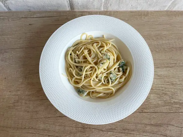 Spaghetti aglio olio z kawałkami sera pleśniowego na białym talerzu.