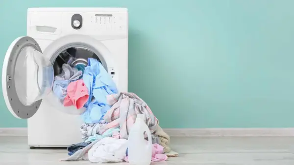 Lavadora blanca con ropa de colores y botella de detergente. Aprende como limpiar la lavadora para un mejor lavado.
