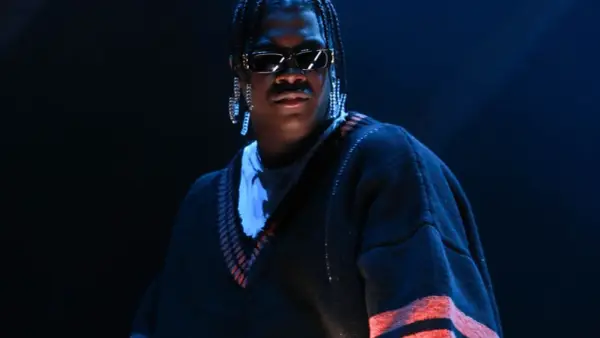 Lil Yachty w okularach i długich kolczykach, w swetrze z pomarańczowymi pasami. Let's start here.