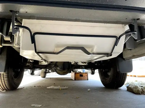 Vue sous un camping-car, montrant le réservoir d'eau propre fixé au châssis. Préparation pour le nettoyage de la cuve camping car.