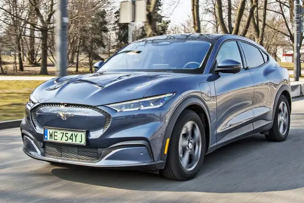 Niebieski Ford Mustang Mach-E jedzie po drodze, z widocznym logo konia na grillu.
