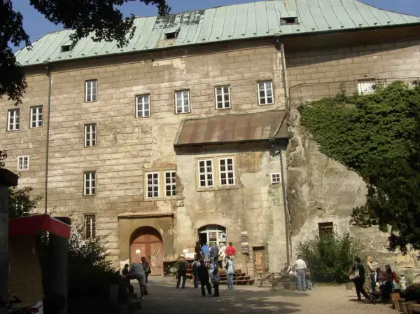 Kamienny zamek Houska z zielonym dachem i licznymi oknami, otoczony zielenią.