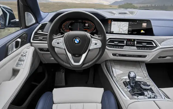 Wnętrze BMW X7: kierownica, ekran multimedialny z nawigacją i muzyką, panel klimatyzacji, dźwignia zmiany biegów.
