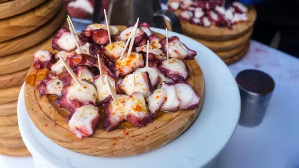 Pulpo a la gallega servido en tabla de madera, con palillos y espolvoreado con pimentón.