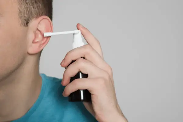 Mężczyzna aplikuje spray do ucha, łagodząc płyn w komórkach wyrostka sutkowatego.