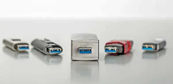 Fünf USB-Sticks in verschiedenen Designs, alle mit blauem Anschluss. Einer davon, der mittlere, wirkt besonders robust, fast wie ein Relikt aus der Zeit der USB 1.0 Geschwindigkeit.