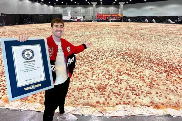 Mężczyzna prezentuje certyfikat Guinnessa za największą pizzę świata, która rozciąga się na ogromnej przestrzeni.