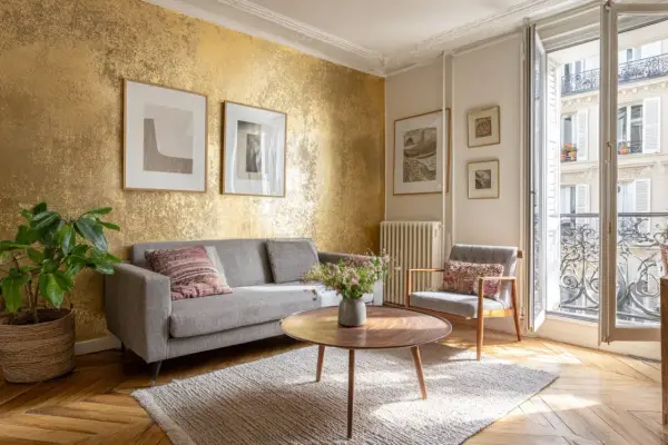 Un salon élégant avec un mur texturé doré, un canapé gris, un fauteuil, une table basse et des tableaux. Une idée pour comment faire du doré avec de la peinture.