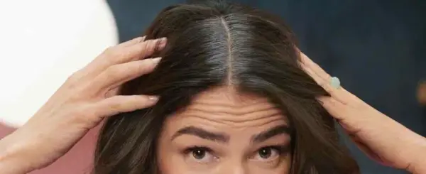 Mujer se toca el cabello oscuro, mostrando cómo disimular las canas en la raya.