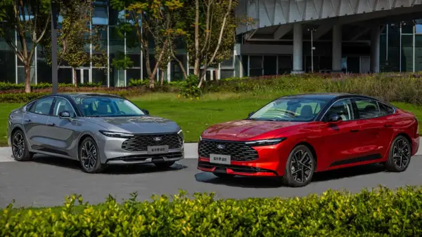 Dwa nowe Fordy Mondeo mk6, jeden czerwony, drugi szary, stoją obok siebie na tle nowoczesnego budynku i zieleni.