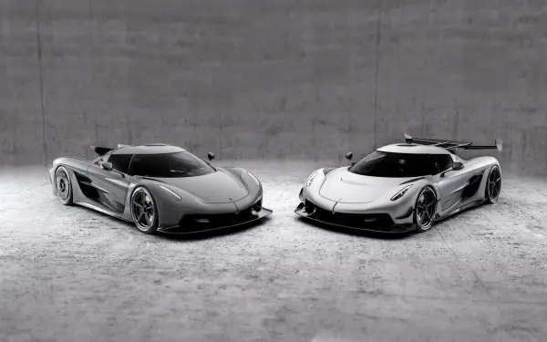 Dwa lśniące Koenigsegg Jesko, jeden szary, drugi srebrny, stoją obok siebie na betonowym tle, gotowe do wyścigu.