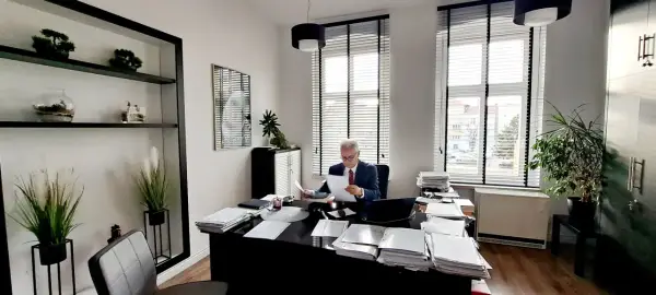 Adwokat w garniturze siedzi przy biurku w gabinecie, przeglądając dokumenty.