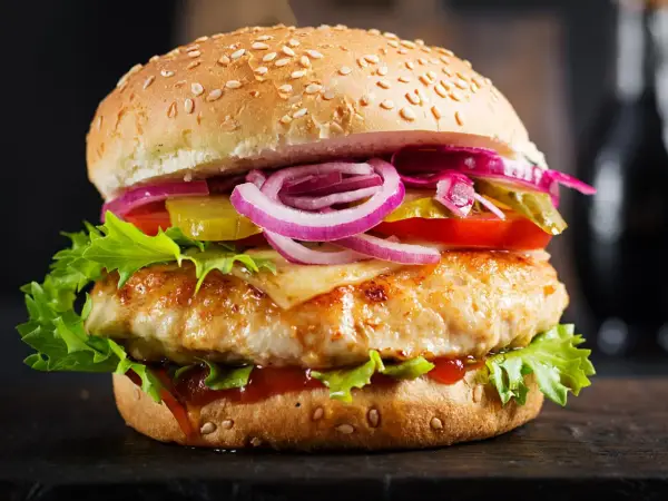 Apetyczny burger drwala podwójny z soczystym kurczakiem, serem, chrupiącą sałatą, pomidorem, ogórkiem i czerwoną cebulą.