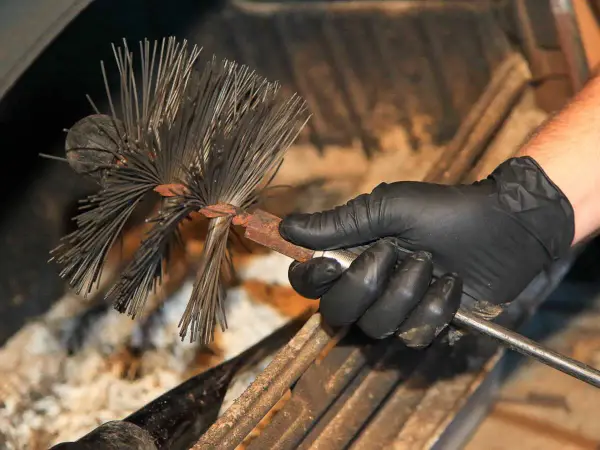 Main d'un ramoneur tenant une brosse pour cheminée. Le ramonage est essentiel pour l'assurance.