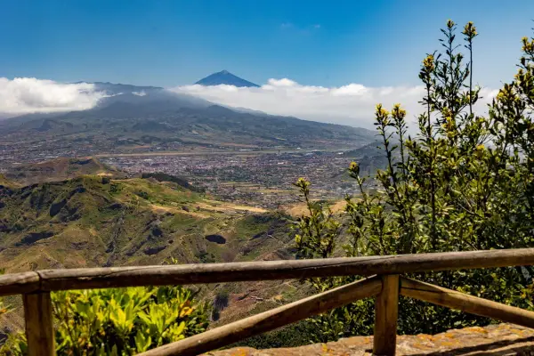 Vista panorámica desde Anaga, Tenerife, con el Teide asomando entre las nubes. Un paisaje verde y montañoso se extiende hasta el mar.