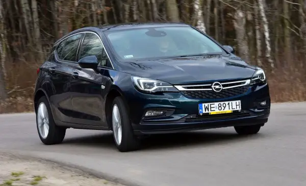 Ciemnozielony Opel Astra K 1.4 Turbo jedzie po drodze wśród drzew.