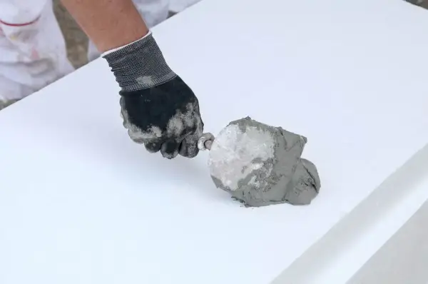 Ręka w rękawicy nakłada klej budowlany w piance na biały styropian.