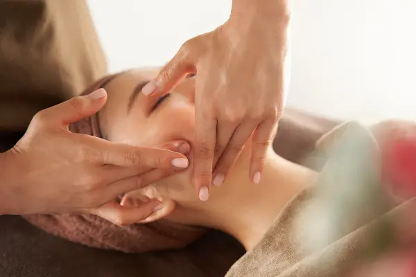 Manos expertas realizan un **dibujo masaje facial paso a paso**, aplicando suaves presiones en el rostro de una mujer para relajarla.