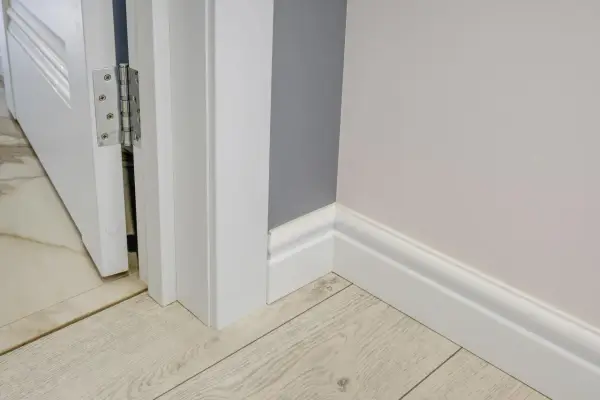 Nymålade vita snickerier runt en dörröppning och längs väggen. Golvet är ljust träliknande laminat.