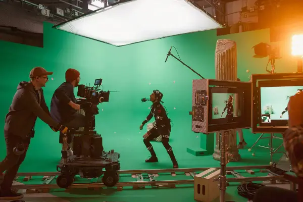 En un set de filmación con pantalla verde, un actor con traje de captura de movimiento interactúa con un equipo de filmación. Esto es vfx que es, la magia del cine.