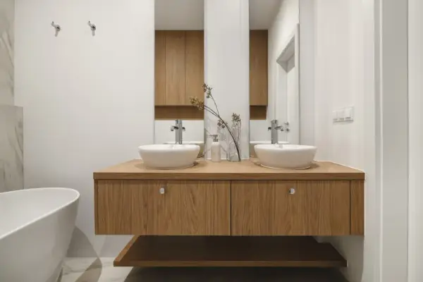 Nowoczesna łazienka z dwoma umywalkami na drewnianej szafce. Minimalistyczny design, białe ceramika i naturalne drewno tworzą harmonię.