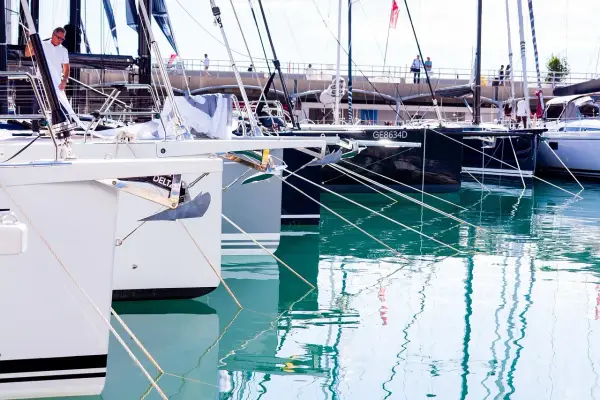 Plusieurs bateaux de plaisance sont amarrés dans un port. La coque du bateau, blanche et grise, est visible au premier plan, avec une ancre argentée.