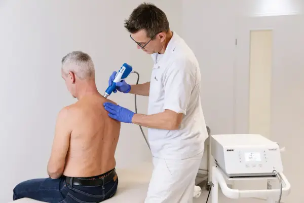 Therapeut behandelt Manns Schulter mit Stoßwellentherapiegerät. Es tut nicht weh, wie eine Spritze in die Schulter.