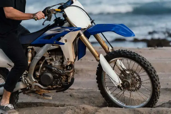 Persona sentada en una moto de cross azul y blanca en la arena, con el mar al fondo. ¿Cuánto paga un desguace por una moto?
