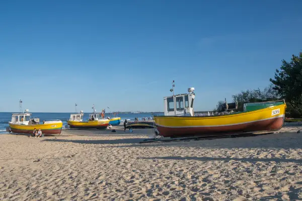 Żółte łodzie rybackie na piaszczystej plaży w Sopocie, spokojne morze i błękitne niebo.
