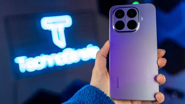 Fioletowy Xiaomi 15T Pro z potrójnym aparatem Leica w dłoni, na tle niebieskiego logo.