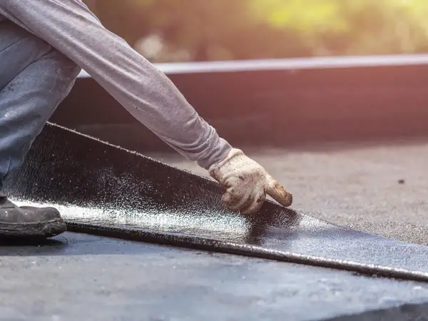 Hand mit Handschuh legt neue Dachpappe an. Alte Dachpappe entsorgen ist wichtig für die Langlebigkeit.