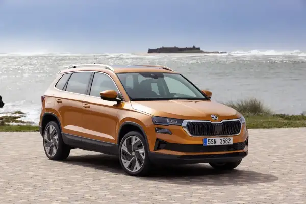 Pomarańczowa Skoda Karoq na tle morza i zamku. Sprawdź aktualny skoda cennik i wybierz swój wymarzony model.
