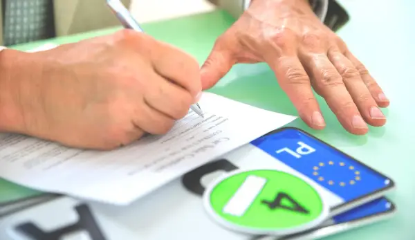 Podpisanie umowy kupna-sprzedaży pojazdu, co jest kluczowe dla uzyskania homologacji. Obok dokumentów leżą tablice rejestracyjne.