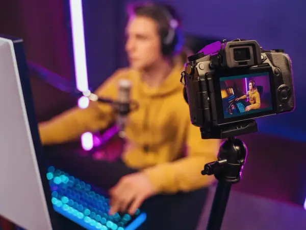 Kamerka do streamowania rejestruje młodego gracza w żółtej bluzie, otoczonego neonowym światłem.