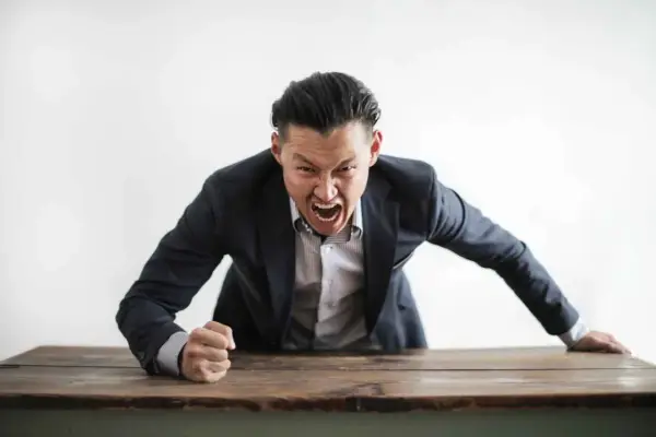 Wütender Mann im Anzug schreit über einen Tisch. Darf ein Lehrer Schüler anschreien?