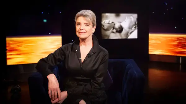 Stina Ekblad sitter i en mörkblå soffa, med en skärm bakom sig som visar klipp från filmer och tv-program med henne.