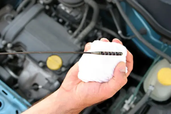 Mano limpiando la varilla del nivel de aceite en el motor. El aceite está entre las marcas de mínimo y máximo.