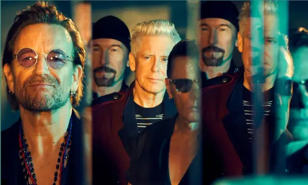 Le groupe U2, avec Bono au premier plan, pose en groupe, leurs visages reflétant une lumière tamisée.